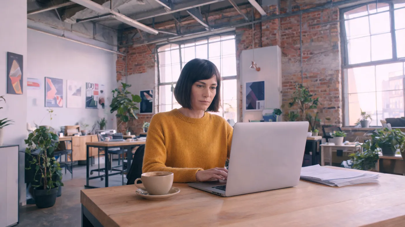 A woman writes on a laptop in a bright office.